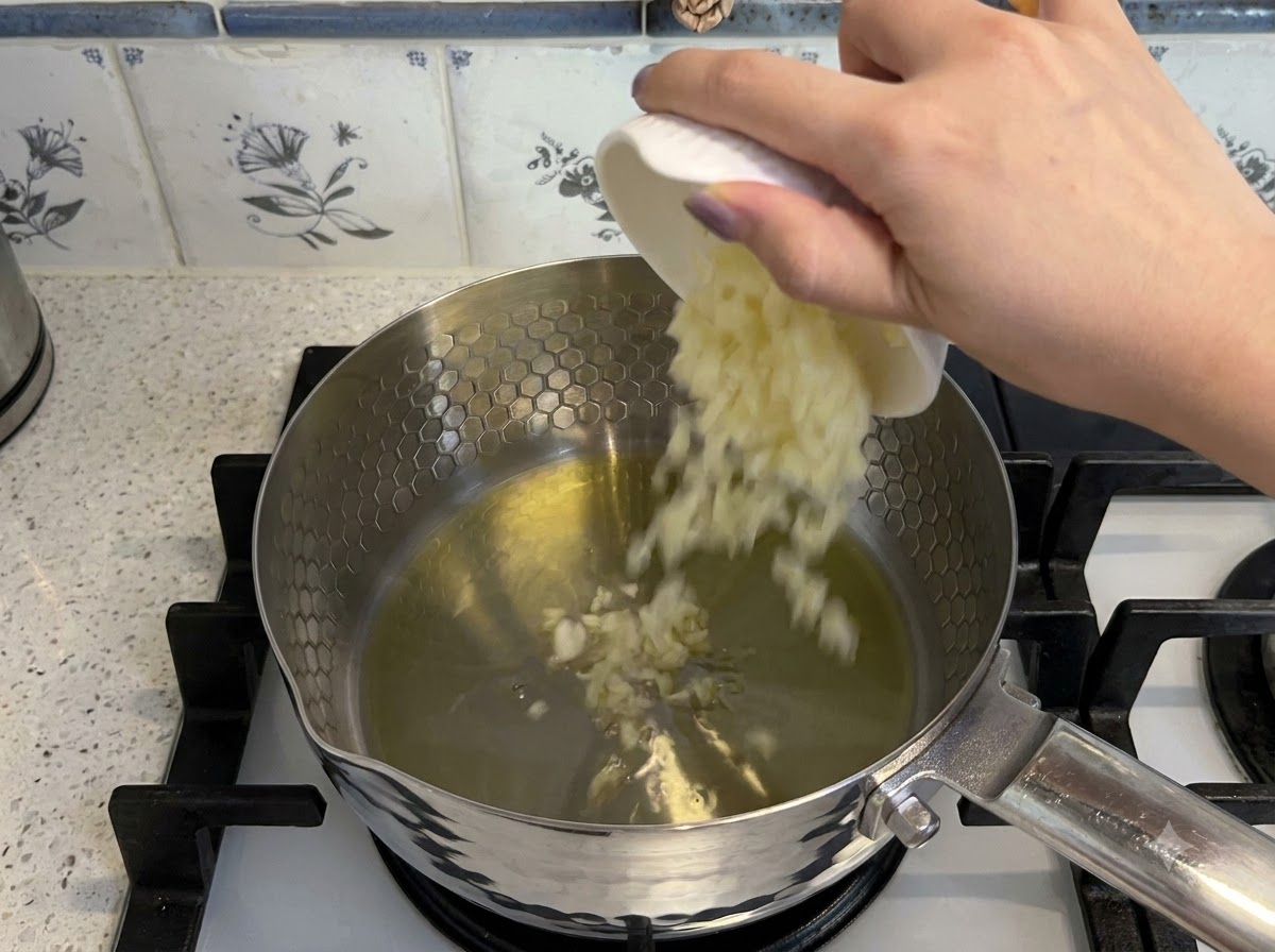 Aglio tritato e pomodori a cubetti aggiunti allolio caldo in una pentola per il soffritto.