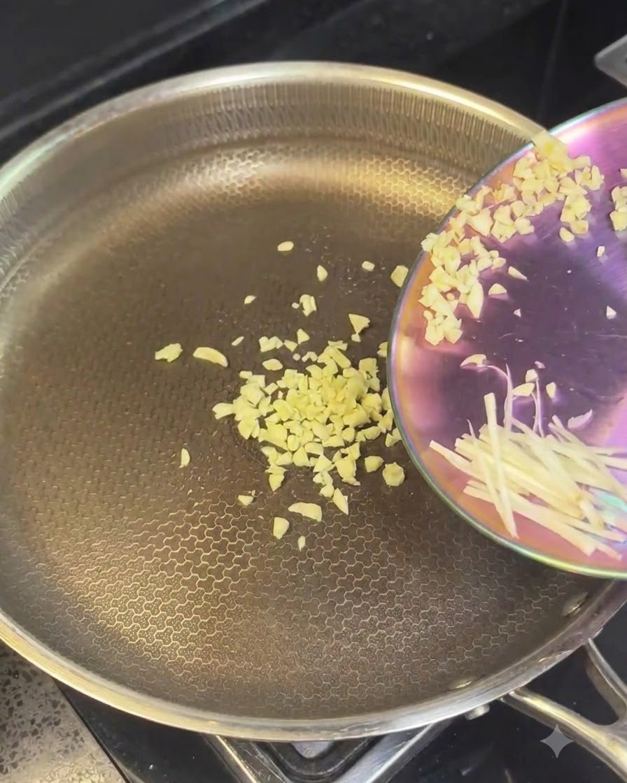 Aglio tritato e cipolle affettate versati in una padella calda di acciaio inossidabile.