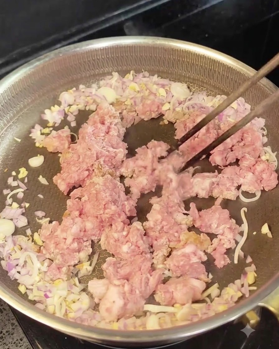 Carne macinata cruda al centro di una padella, circondata da cipolle e aglio soffritti.