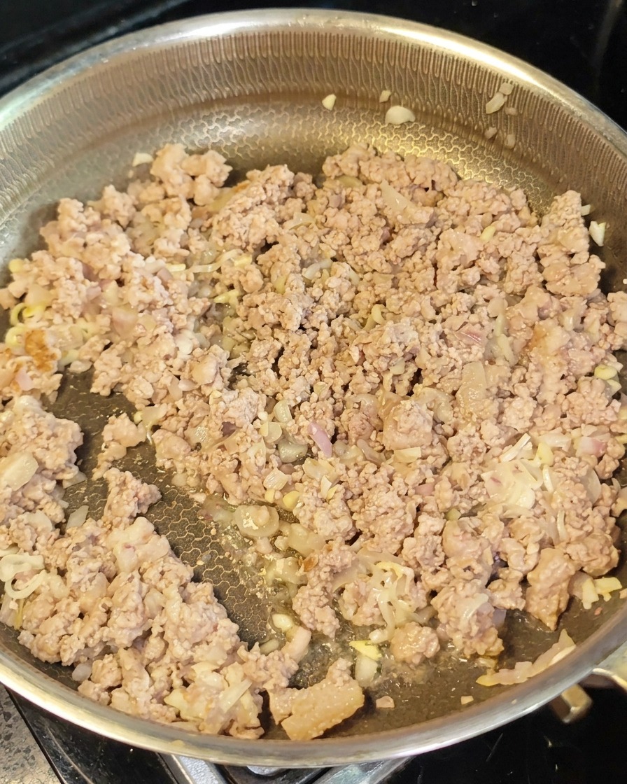 Carne macinata rosolata e aromi distribuiti in padella mentre viene incorporata la pasta di miso rosso.