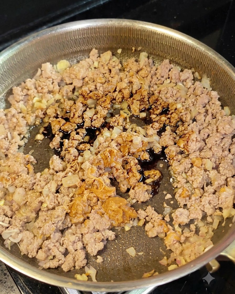 Salsa di soia scura versata da un piccolo cucchiaio su carne macinata e cipolle in padella.