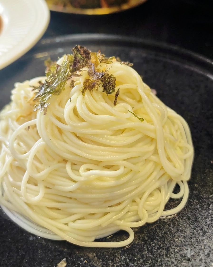 Fiocchi di alghe essiccate tritati sparsi su un mucchietto a spirale di noodles ramen cotti su un piatto scuro.