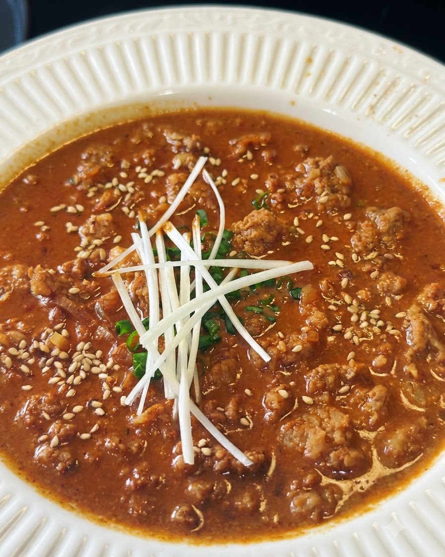Semi di sesamo bianco tostati sparsi su una ciotola di salsa di carne saporita guarnita con cipollotti.