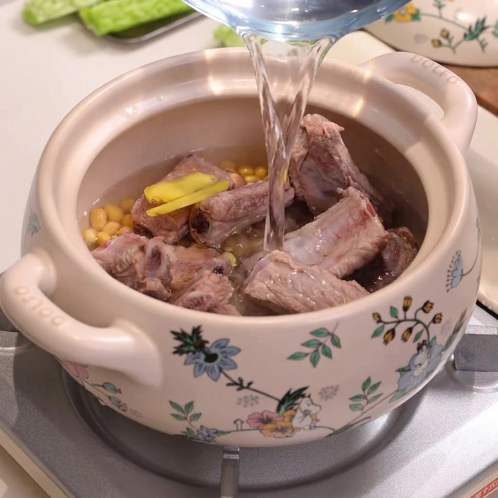 Lacqua viene versata da una caraffa in una pentola di ceramica decorata piena di costine di maiale e soia.