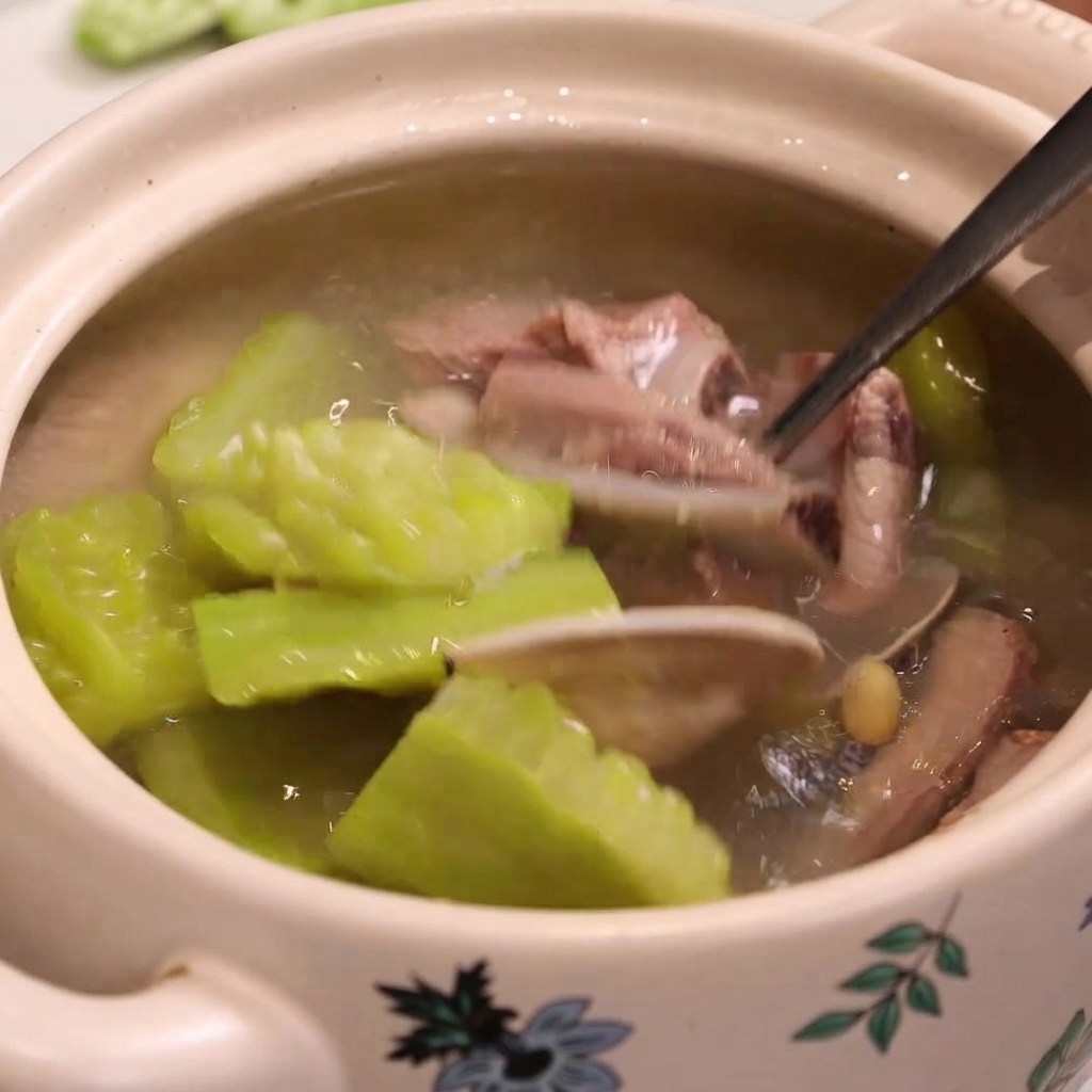 Un cucchiaio di metallo raccoglie costine cotte, vongole e melone amaro da una pentola.