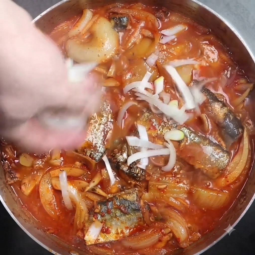 Cipollotti bianchi tritati cosparsi sopra una pentola di pesce brasato in ebollizione.