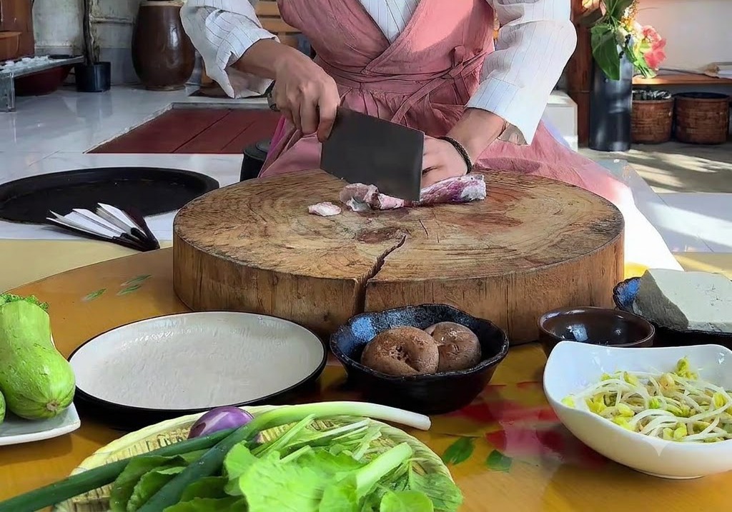 Mani che usano una mannaia per affettare la pancetta cruda su un grande tagliere rotondo di legno.