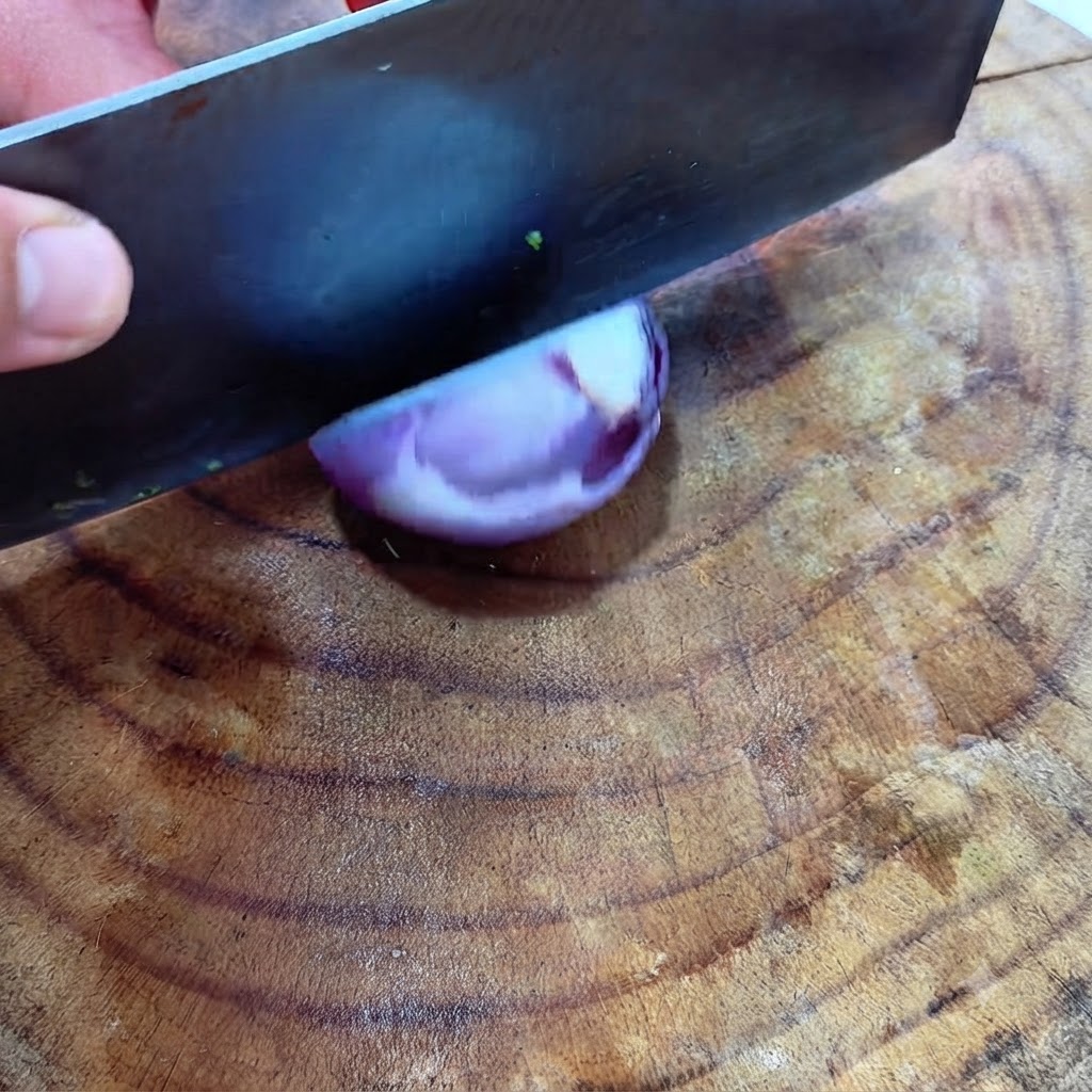 Una grande mannaia che taglia a dadini mezza cipolla rossa su una superficie di legno.