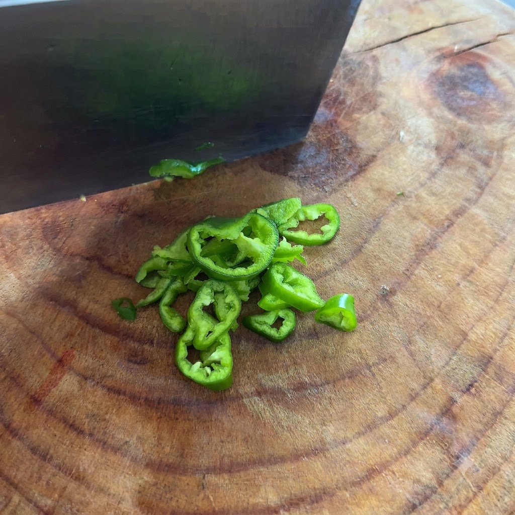 Peperoncini verdi affettati in anelli sottili con un coltello su un tagliere.
