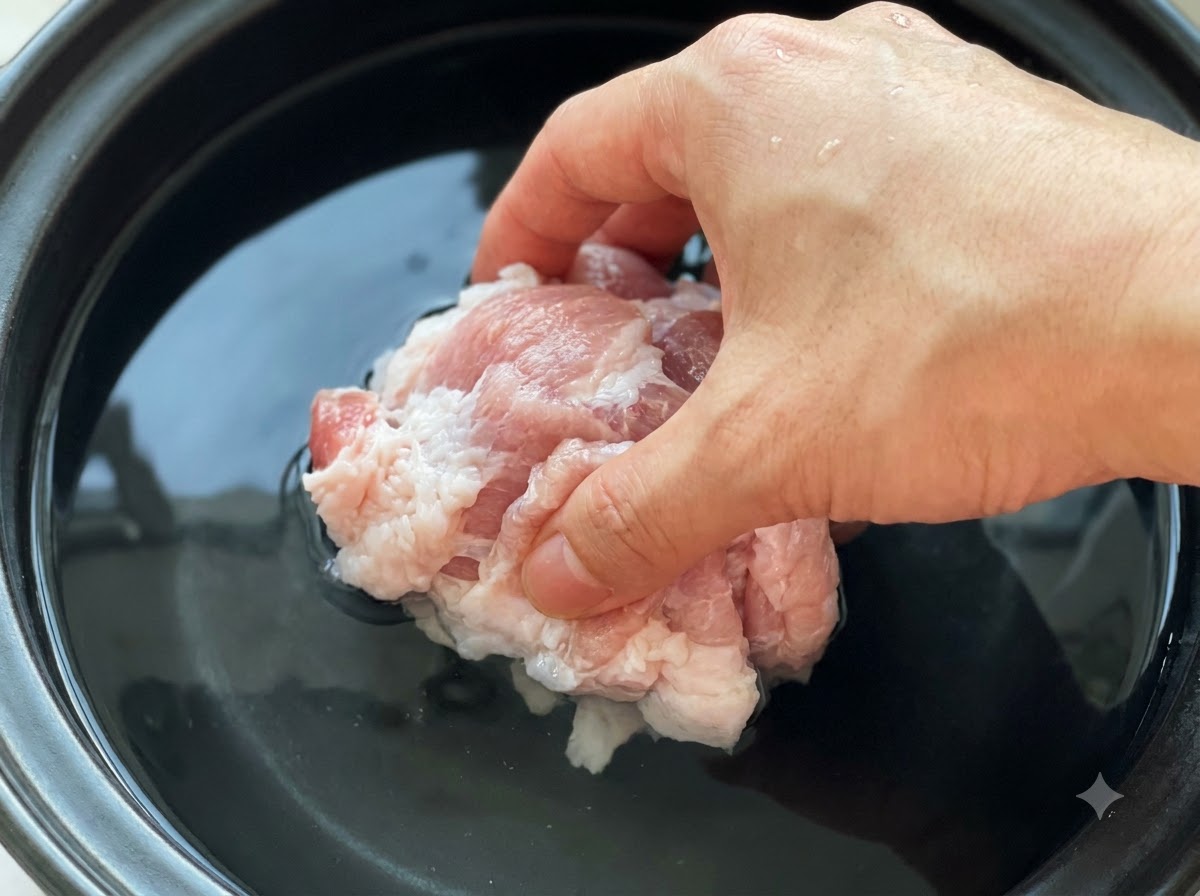 Pezzi di maiale crudo immersi in una pentola piena di acqua fredda e pasta di soia.