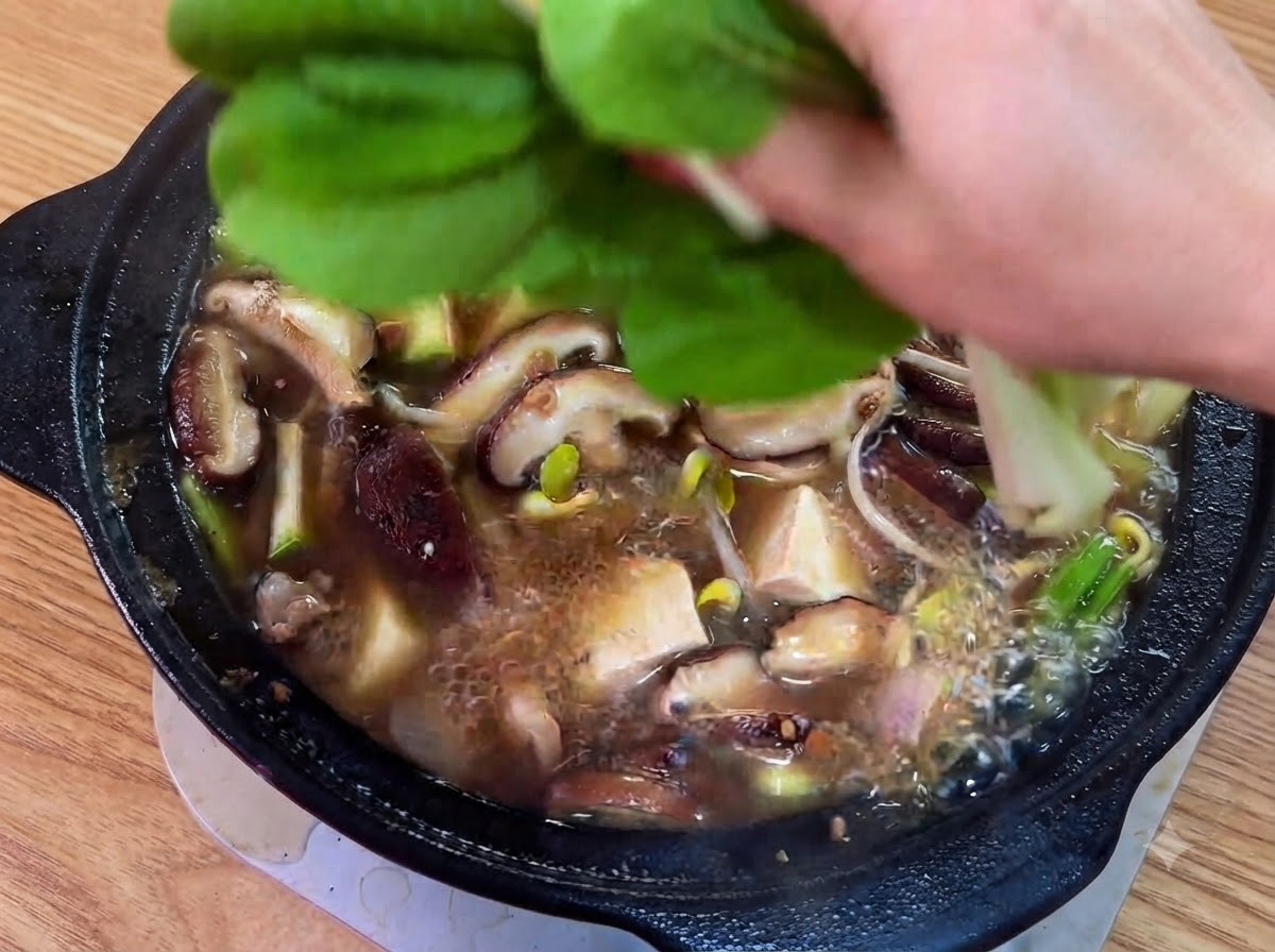 Foglie verdi fresche e peperoncini verdi a fette posizionati in cima allo stufato in cottura.