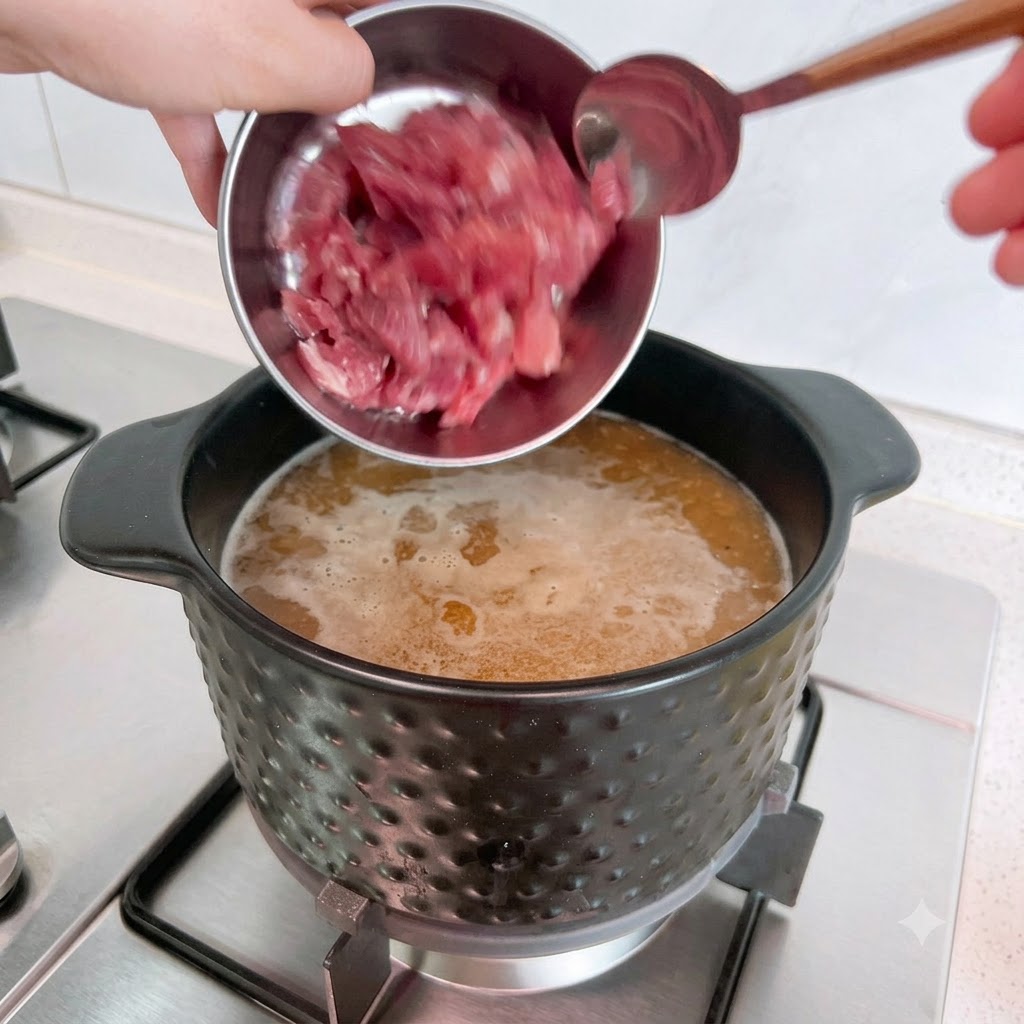 Pezzi di maiale crudo vengono versati da una ciotola di metallo in una pentola di brodo bollente.