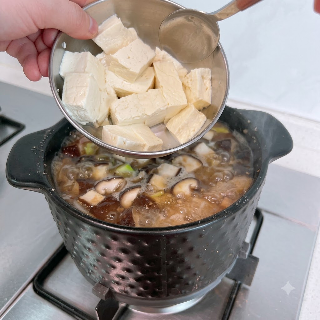 Fette di tofu bianco vengono aggiunte da una ciotola di metallo nello stufato che bolle.