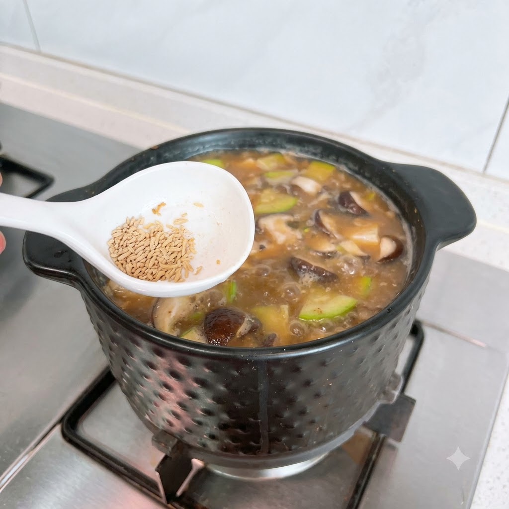 Un cucchiaio bianco con del dado di manzo in polvere tenuto sopra una pentola bollente di Doenjang Jjigae.