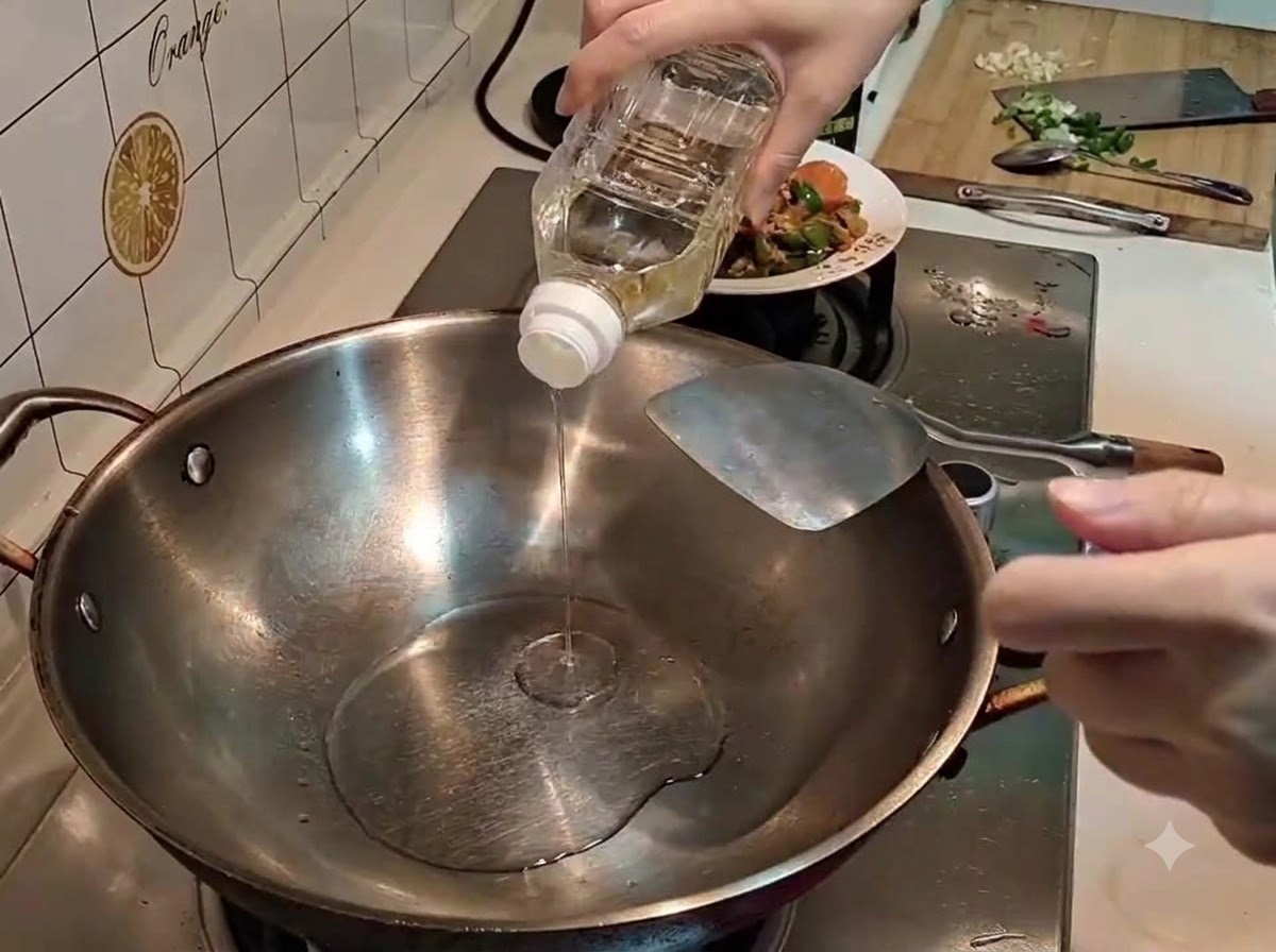 Una mano versa olio trasparente da una bottiglia di plastica in un wok di acciaio inossidabile caldo.