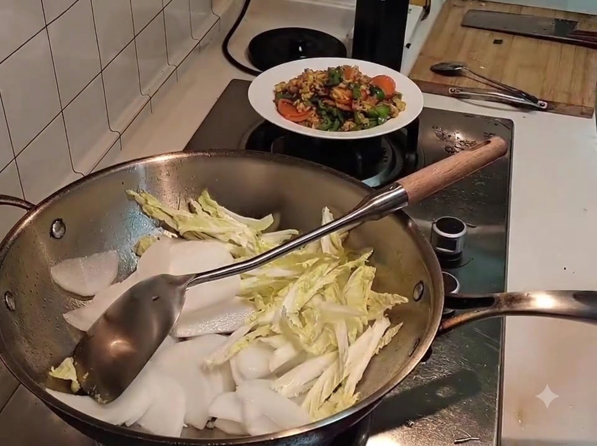 Daikon a fette sopra del cavolo napa leggermente appassito allinterno di un wok di metallo, con una spatola vicina.