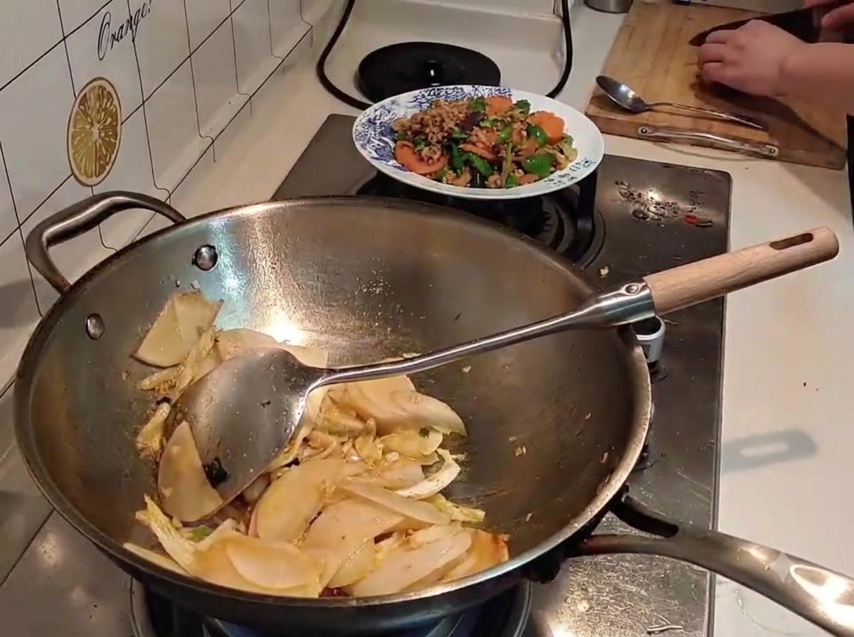 Acqua versata da un bollitore nero in un wok pieno di ravanello e cavolo saltati.