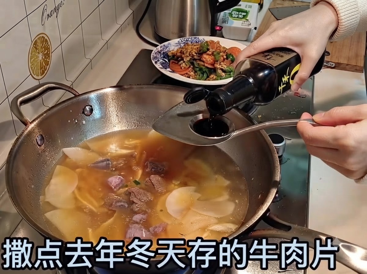 Salsa di soia versata in un brodo bollente contenente fettine di manzo e verdure.