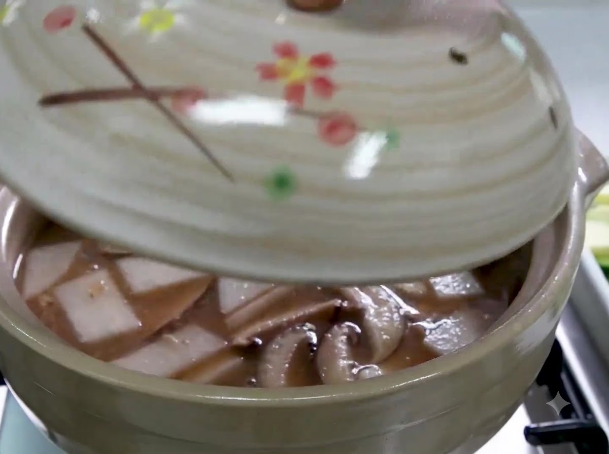 Una mano che posiziona un coperchio su una pentola di ceramica riempita di brodo, ravanello affettato e funghi shiitake.