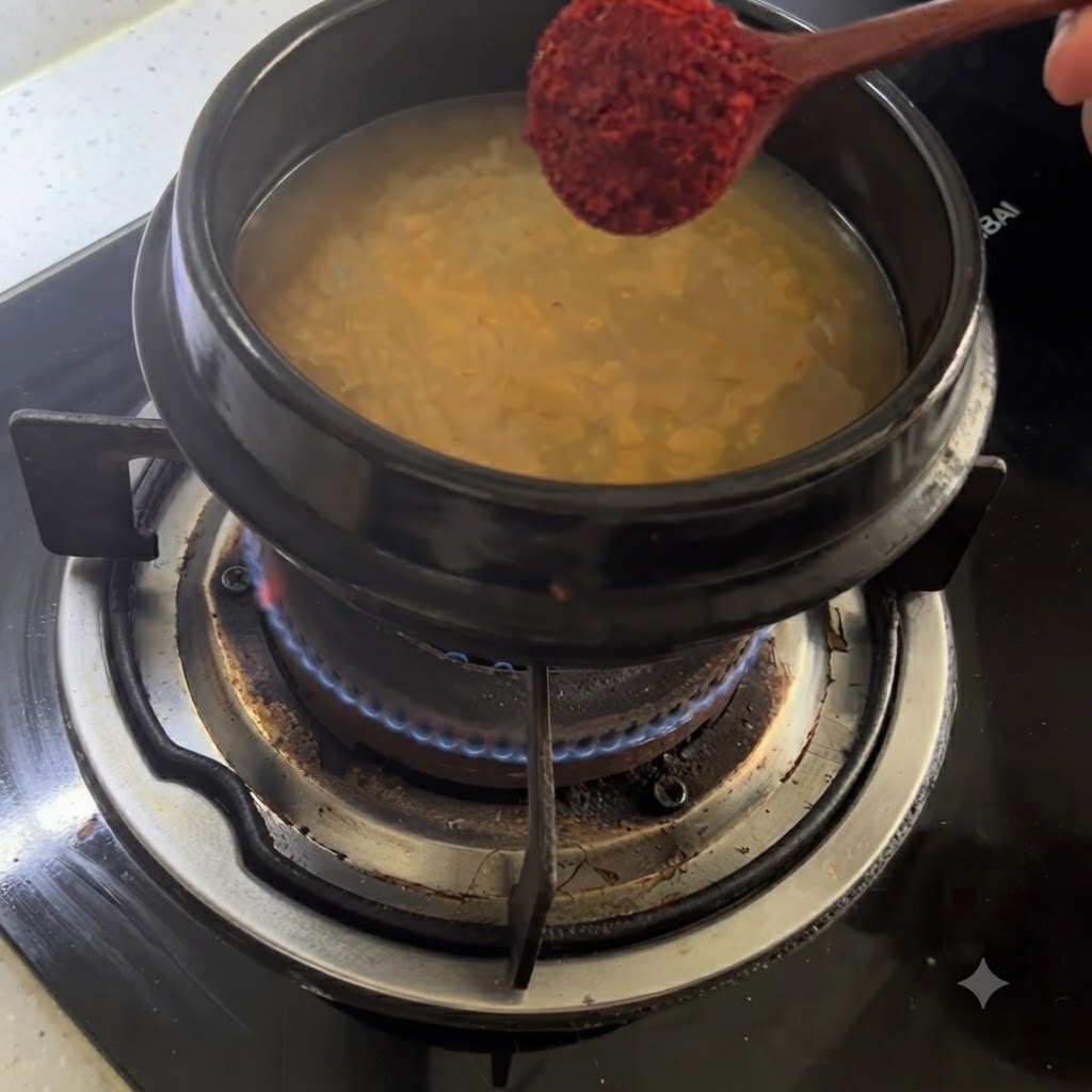 Un cucchiaio di legno che sostiene il peperoncino rosso in polvere sopra una pentola di brodo condito.
