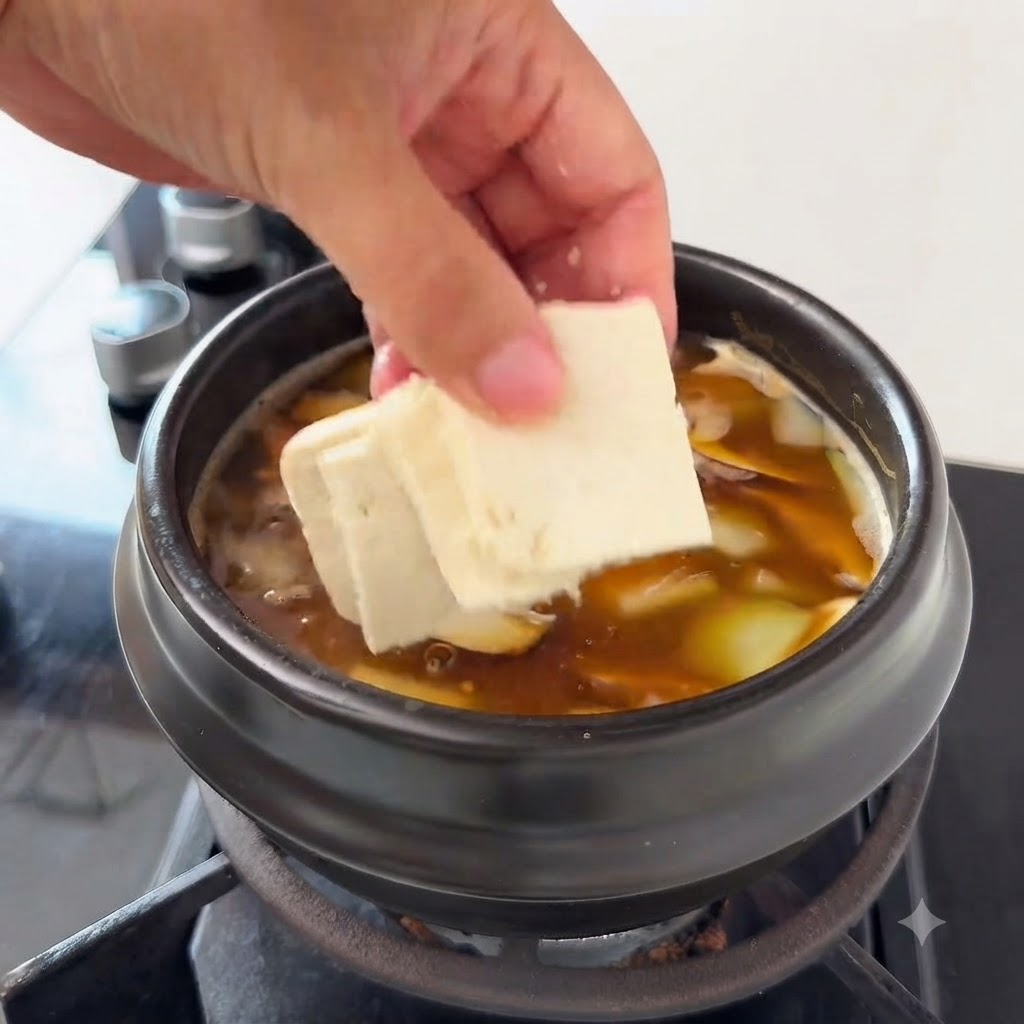 Pezzi di tofu aggiunti alla zuppa contenente fette di zucchina e funghi enoki.
