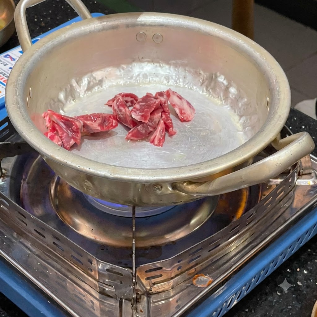 Pezzi di manzo crudo saltati in una piccola pentola di metallo sopra un fornello a gas portatile acceso.