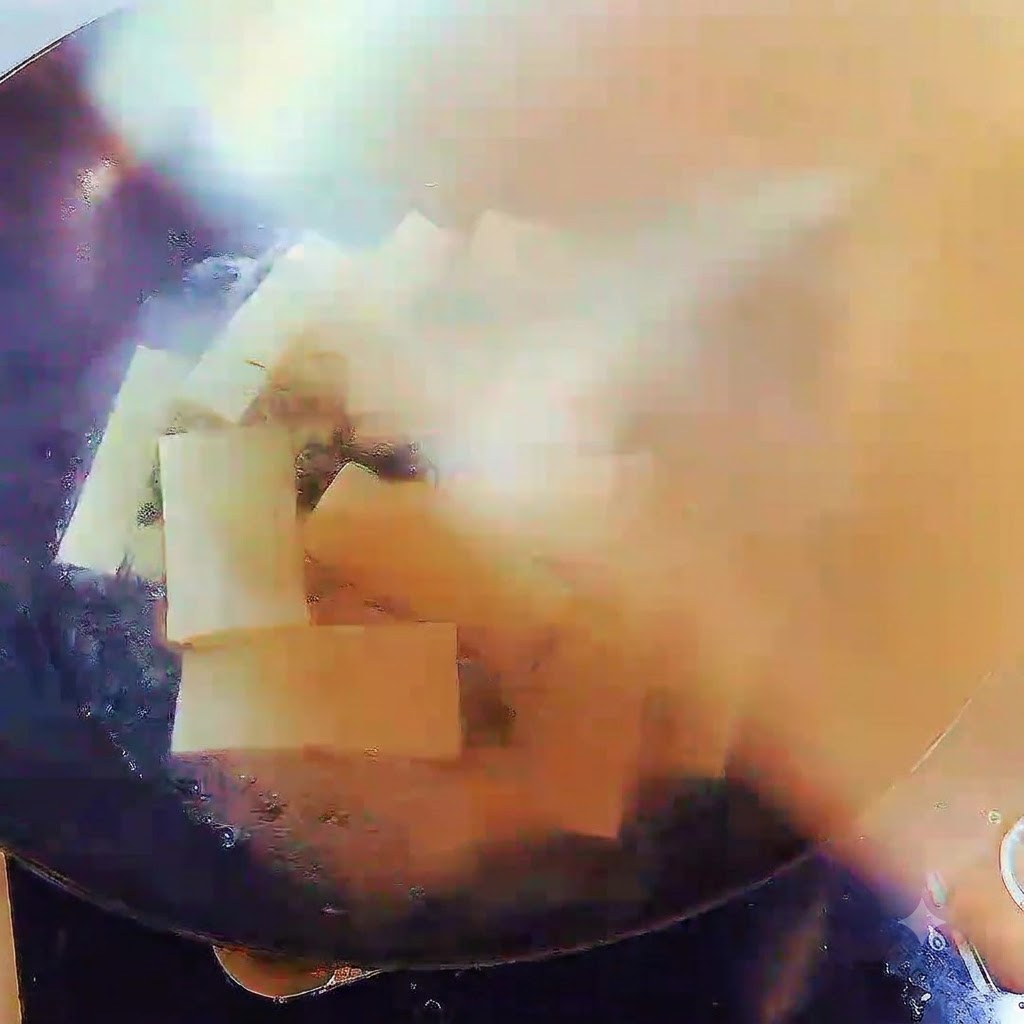 Un wok pieno di zuppa bollente e strisce di tofu, coperto saldamente con un coperchio.