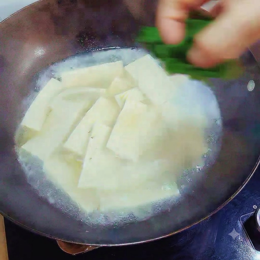 Una mano che fa cadere cipollotti verdi tritati sopra la zuppa di tofu finita nel wok.