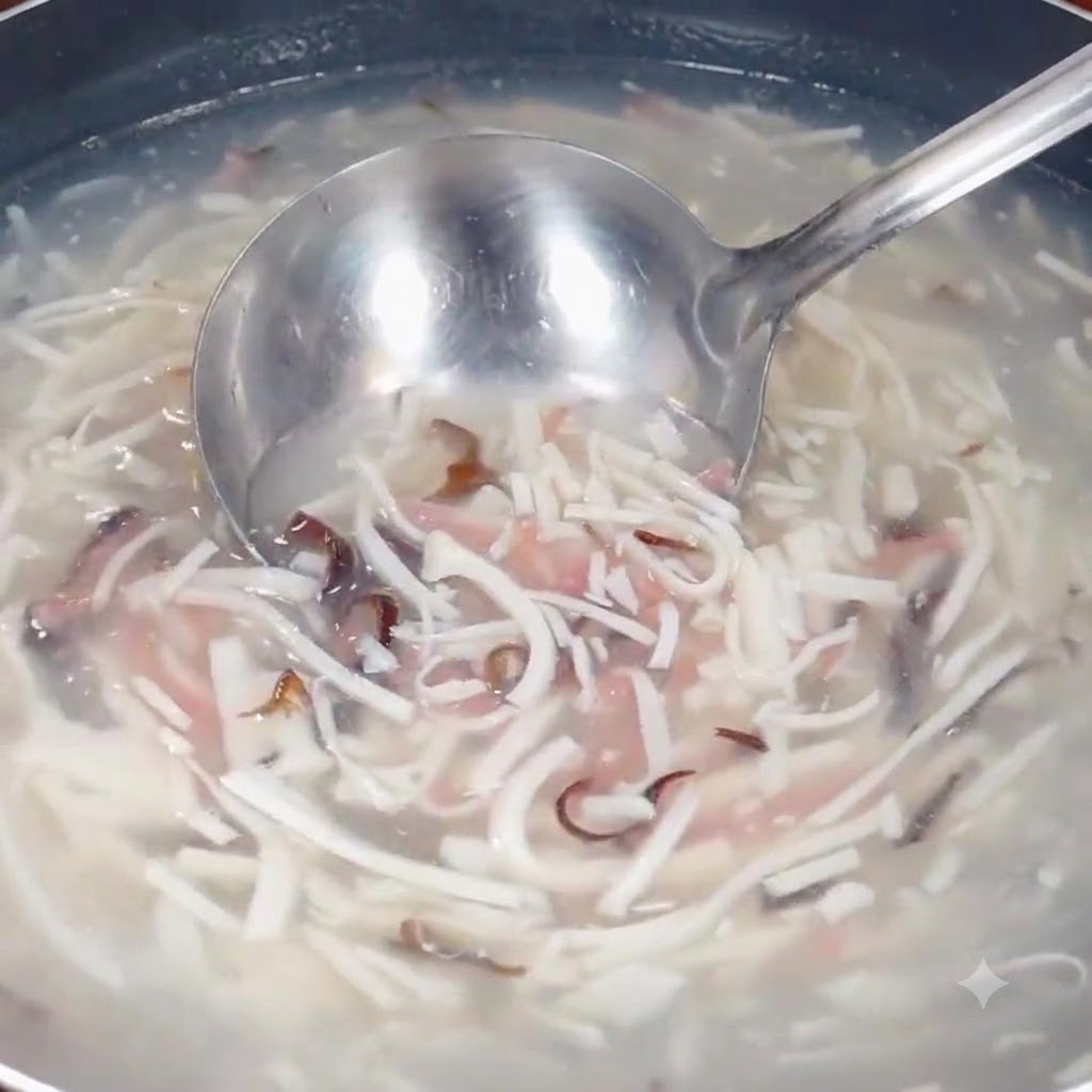 Un mestolo immerso nella zuppa in ebollizione con gli ingredienti a striscioline in una pentola.