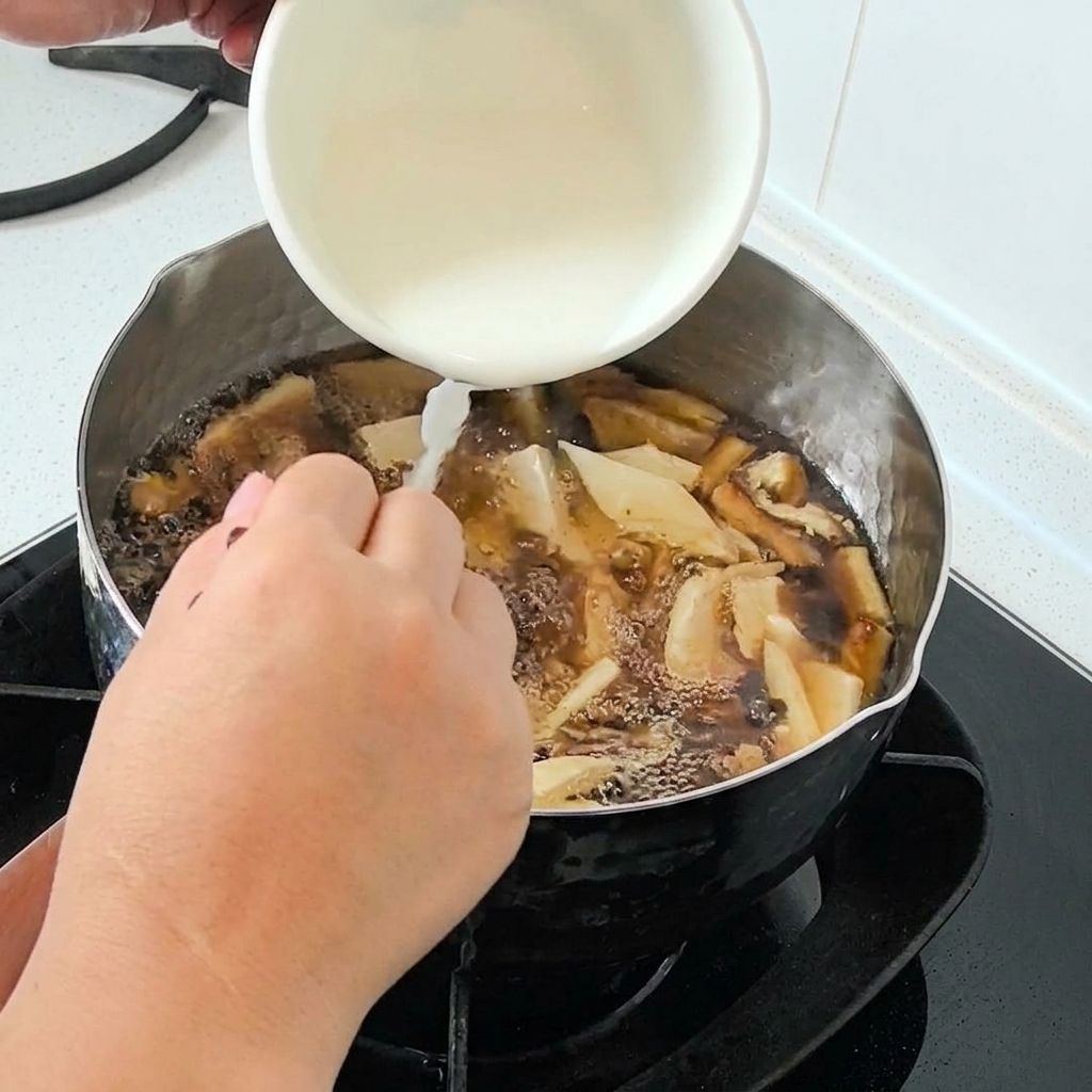 Acqua e amido versati da una ciotola bianca in una pentola di zuppa che bolle.