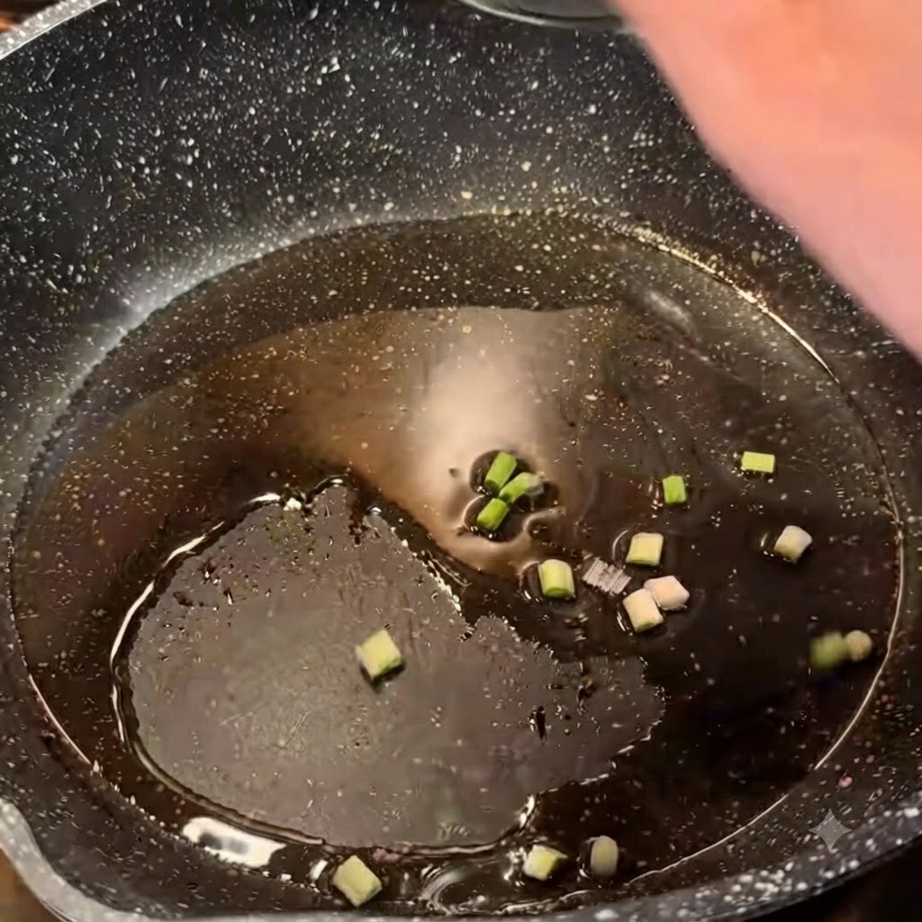 Cipolle verdi tritate che sfrigolano nellolio caldo allinterno di una padella scura.
