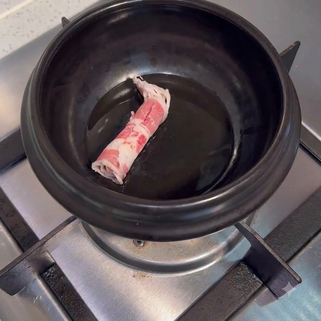 Fettine di manzo crude posizionate allinterno di una pentola di ceramica nera con olio su un fornello.