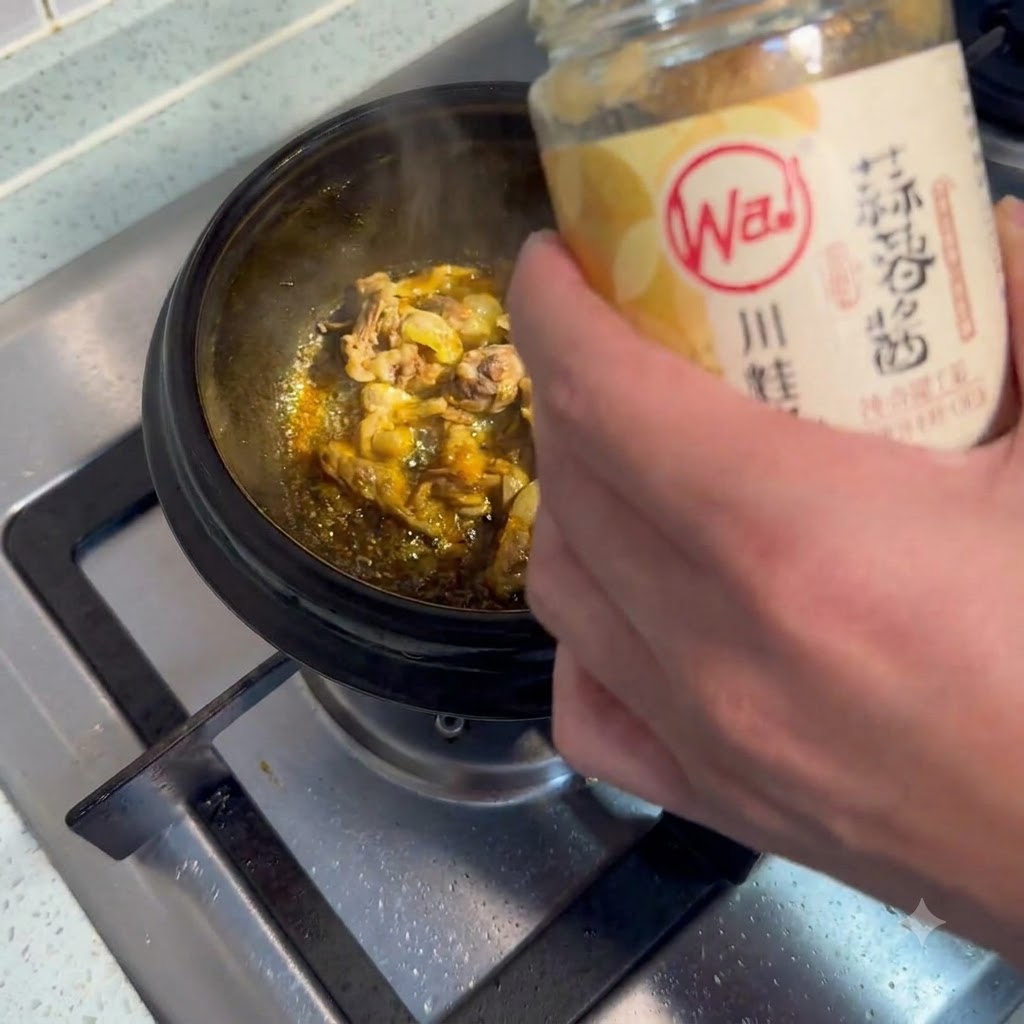 Un cucchiaio di pasta daglio prelevato e aggiunto in una pentola di carne sfrigolante.