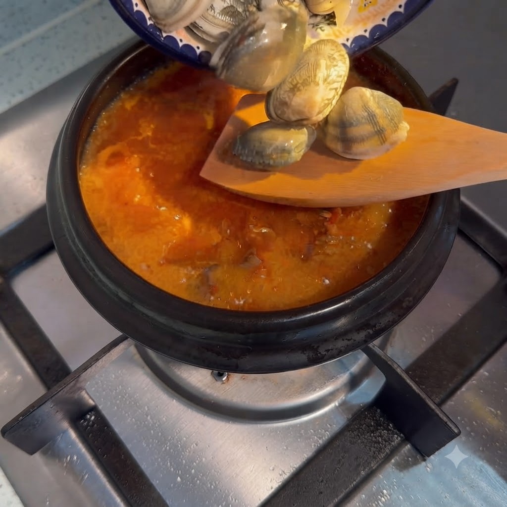 Vongole fresche versate da un piattino in una pentola bollente di zuppa di tofu morbido coreana.