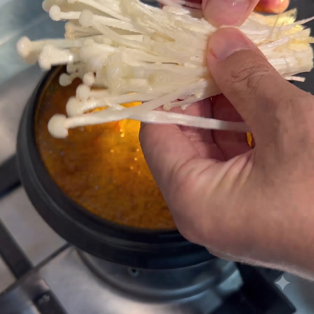 Funghi enoki tenuti in mano e calati nella pentola di zuppa in ebollizione.