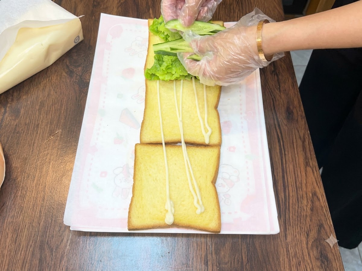 Mani che sistemano fette di cetriolo verde fresco su un letto di lattuga sopra una fetta di pane.