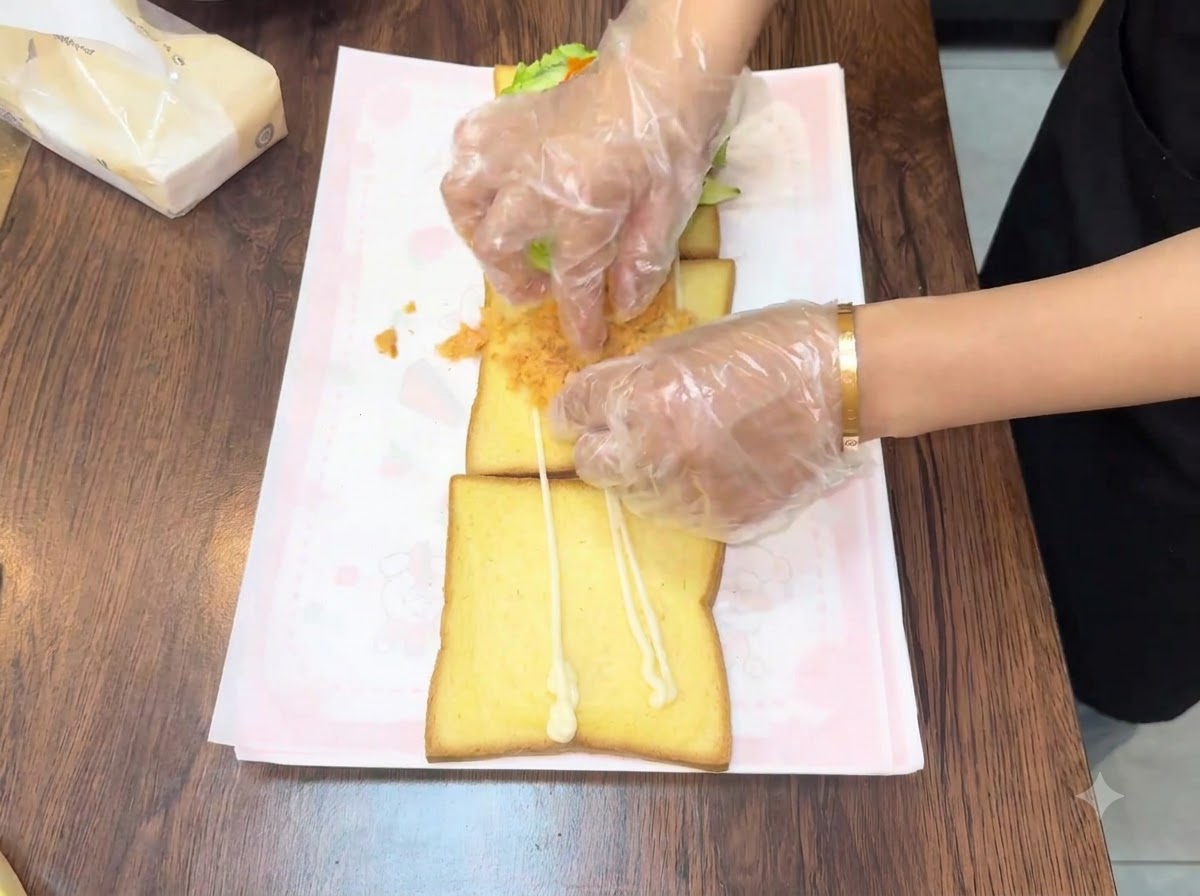 Mani che spalmano floss di carne dorato e soffice sulla seconda fetta di pane.
