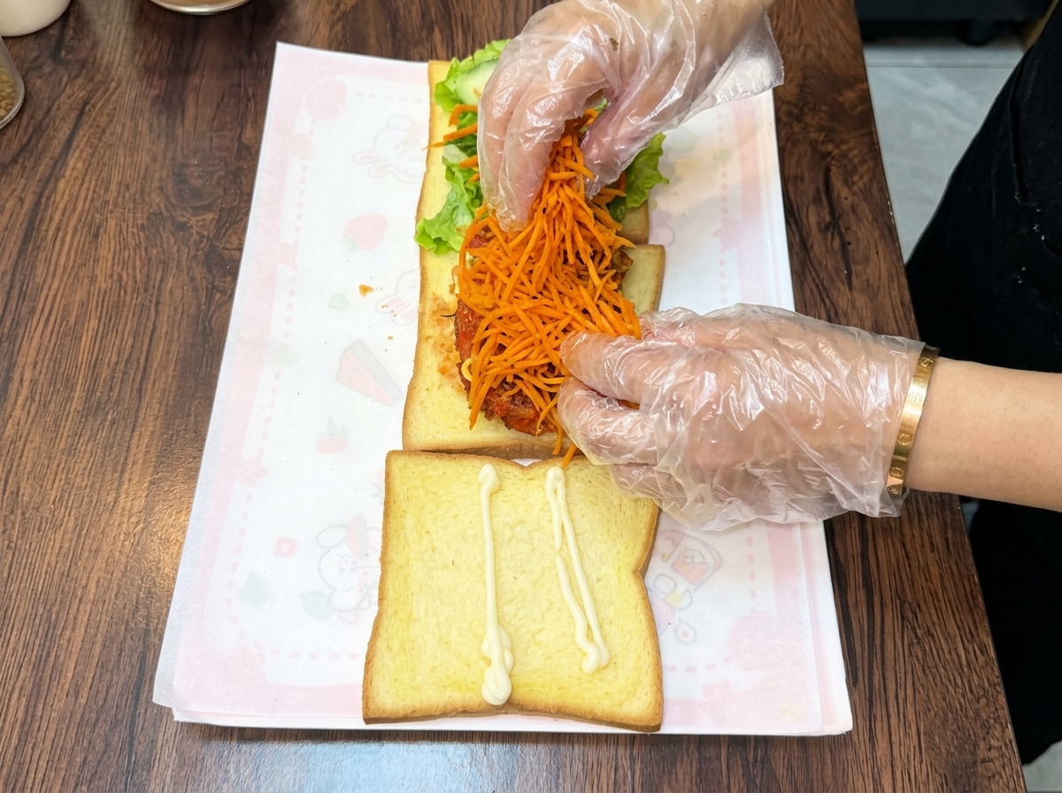 Mani guantate che accumulano un mucchio generoso di carote julienne saltate arancioni brillanti sopra la cotoletta di pollo impilata.