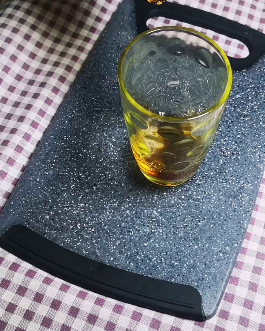 Salsa di soia scura versata in un contenitore di vetro trasparente su un tagliere grigio.