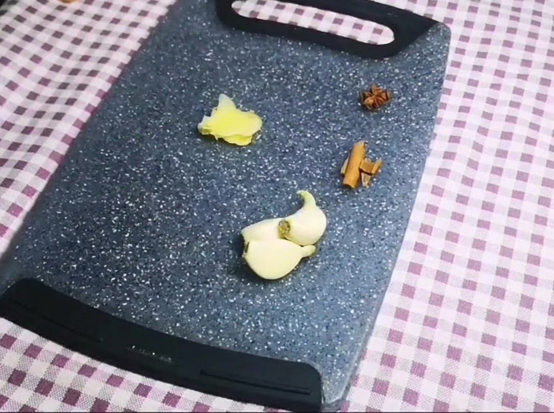 Anice stellato, un bastoncino di cannella, spicchi daglio e zenzero affettato disposti ordinatamente su un tagliere grigio.