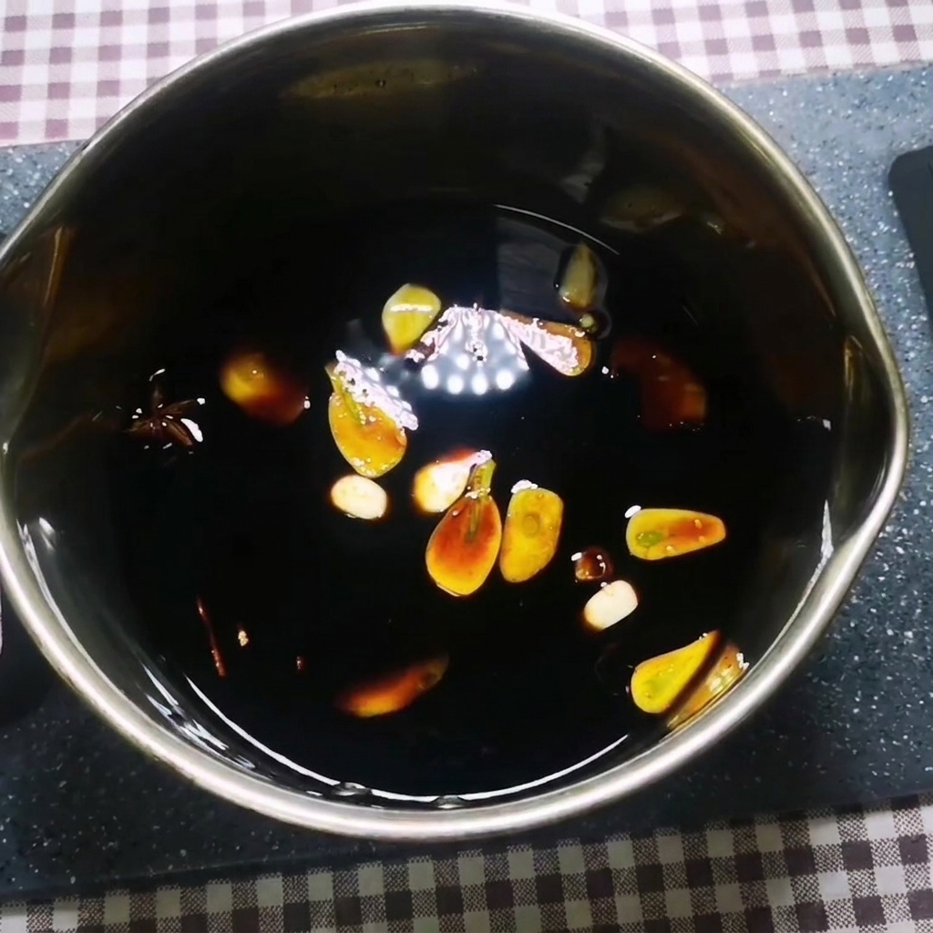 Una salsa scura che sobbolle in una pentola di metallo con aglio, zenzero, anice stellato e cannella che galleggiano allinterno.