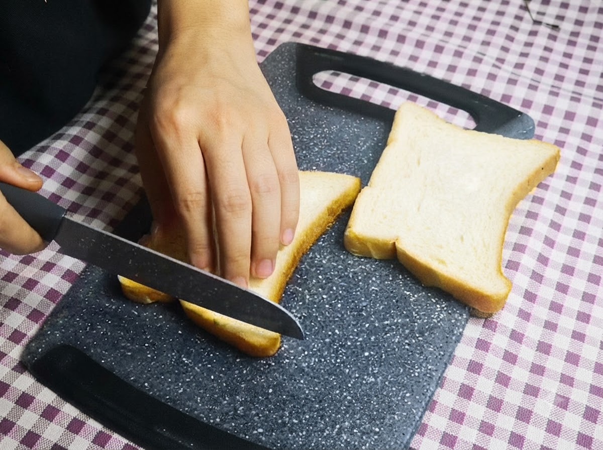 Una persona che usa un coltello per tagliare i bordi delle fette di pane bianco su un tagliere.