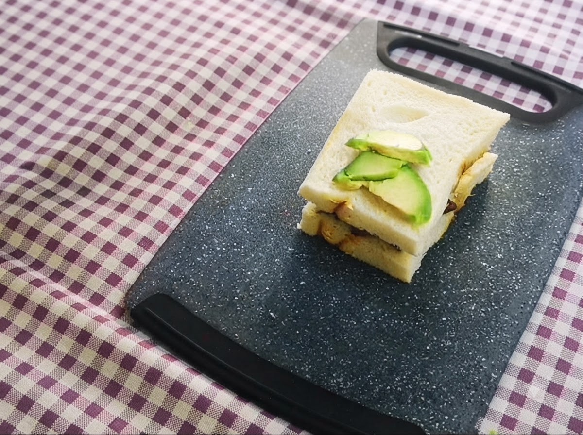 Un sandwich a strati con avocado affettato posto sopra, adagiato su un tagliere.