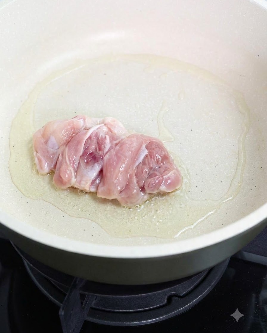 Una coscia di pollo cruda che frigge dal lato della pelle in una padella unta.