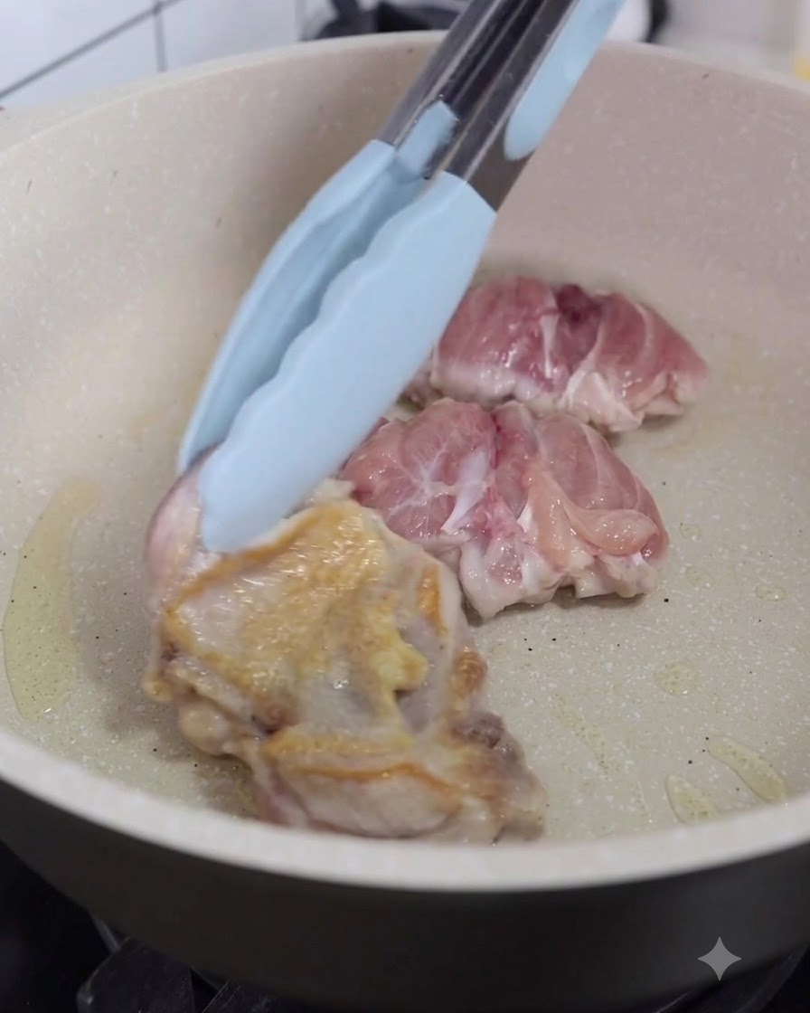 Pezzi di pollo girati nella padella usando pinze da cucina.