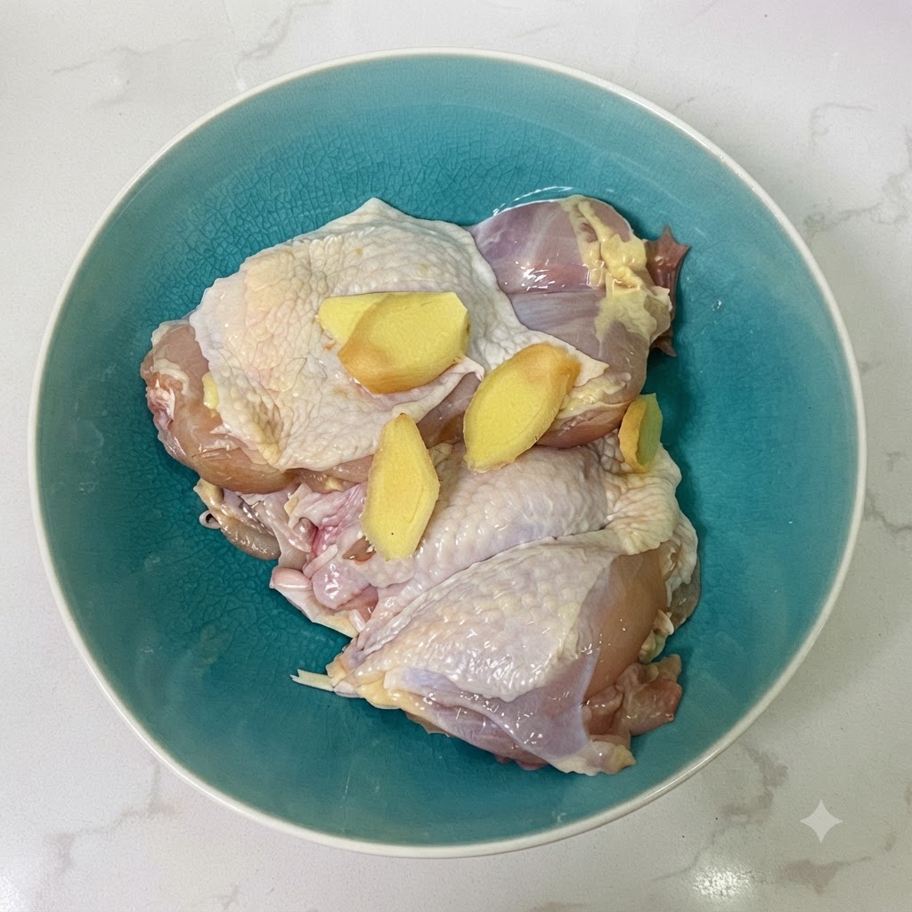 Pezzi di pollo e fette di zenzero in una ciotola di ceramica blu con salsa di soia.