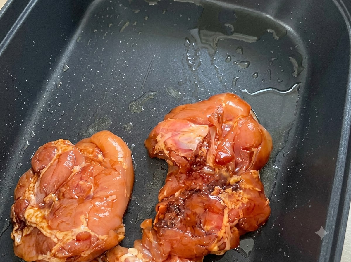 Pezzi di pollo marinato disposti con la pelle rivolta verso il basso in una padella antiaderente nera leggermente unta.
