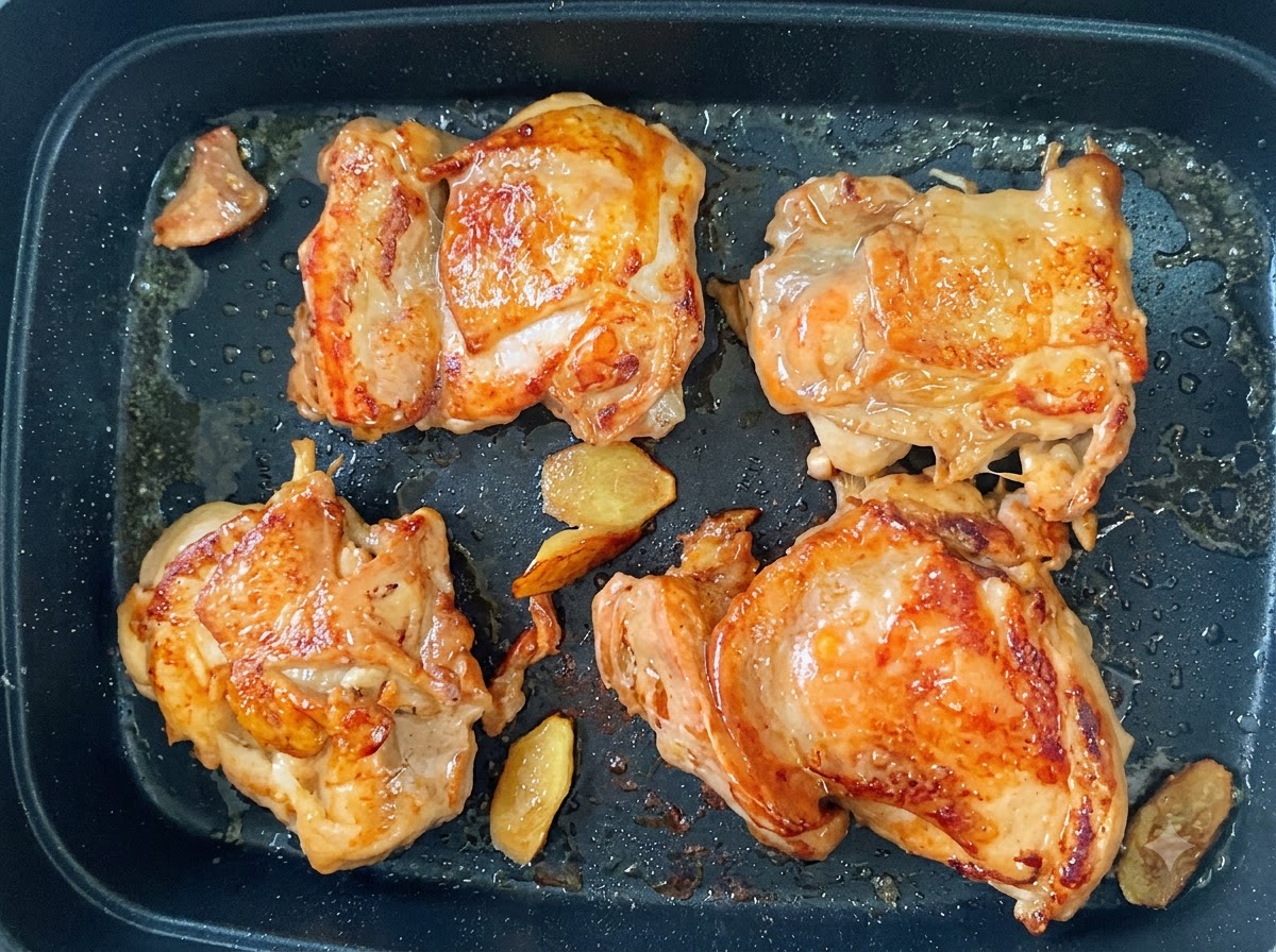 Quattro sovracosce di pollo in padella con una pelle dorata e croccante e fettine di zenzero.