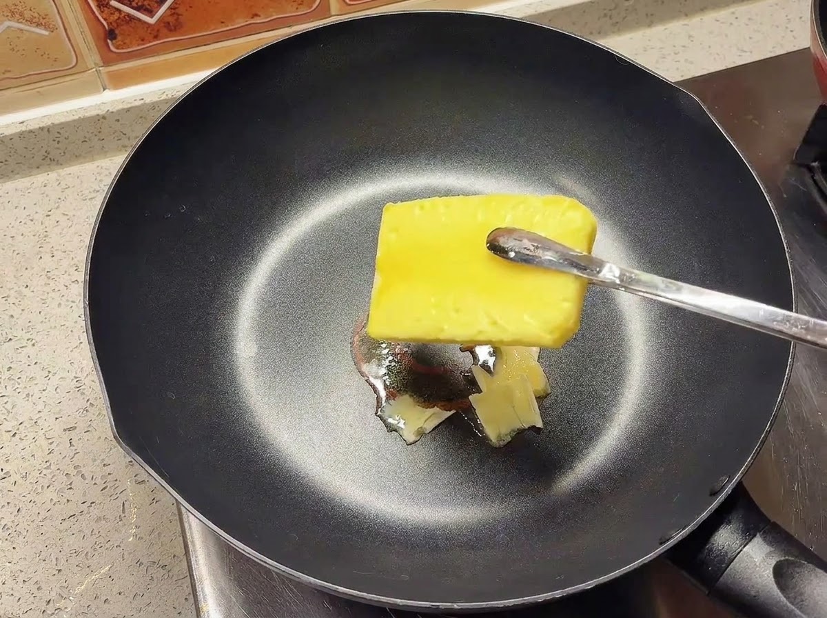 Un panetto di burro giallo che si scioglie in una padella nera calda.
