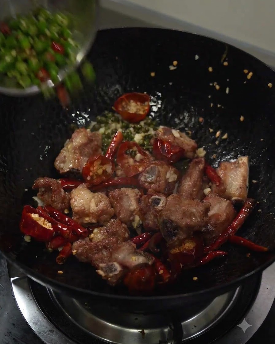 Peperoncini verdi affettati versati nel wok con le costine e gli aromi.